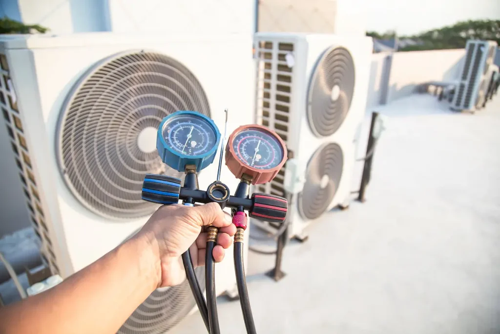 Heat pump technician holding a pressure gauge meter in front of operating heat pump.