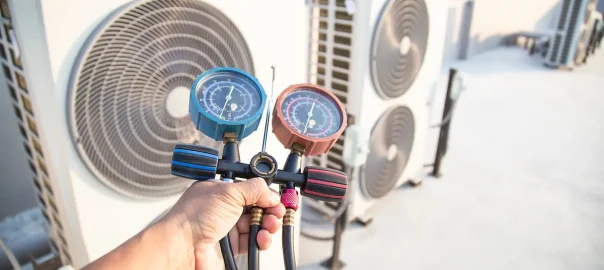 Heat pump technician holding a pressure gauge meter in front of operating heat pump.