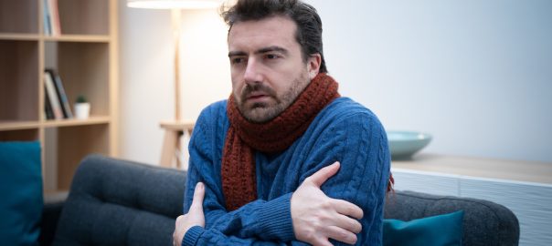 man wearing sweater and scarf, shivering in his home