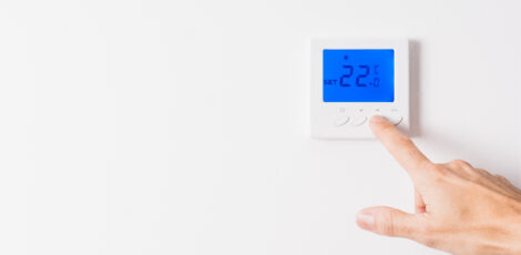 Caucasian man's hand adjusting the temperature of a white thermostat to twenty-two degrees with the blue backlit display on a white wall